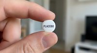 Hand holding white placebo pill tablet between fingers in medical research laboratory setting for clinical trial studies.