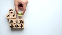 Hand selecting green leaf symbol from wooden blocks with energy icons representing sustainable power choices and environmental responsibility.