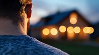 Young man looking at illuminated house with glowing bokeh lights during sunset, creating peaceful evening atmosphere with soft focus background.