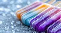 Colorful frozen popsicles lined up on crushed ice background with vibrant purple, turquoise, orange, and pink hues creating refreshing summer treat composition.