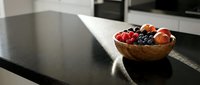 Wooden bowl filled with fresh mixed berries including strawberries and blueberries on modern kitchen countertop with natural light.