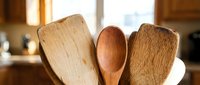 Wooden kitchen utensils including spoons and spatulas in ceramic holder on counter. Natural bamboo and wood cooking tools for culinary preparation.