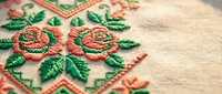 Traditional folk embroidery with vibrant red and green floral roses pattern on natural linen fabric showcasing detailed needlework craftsmanship for textile design.