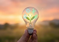 Eco-friendly lightbulb with green plant and renewable energy icons held against sunset sky representing sustainable innovation and environmental solutions.
