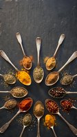 Colorful spices and herbs arranged in wooden spoons on dark slate background for culinary cooking and seasoning recipes.