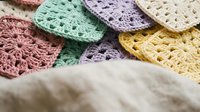 Colorful handmade crochet granny squares in pastel tones arranged on neutral fabric background for crafting and textile projects.