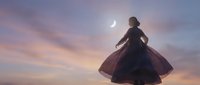 Woman in flowing dress dancing under crescent moon at twilight with dramatic purple and pink sky clouds creating magical atmospheric scene for wellness content.