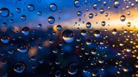 Raindrops on glass window with blurred blue and golden sunset bokeh background, creating a moody, atmospheric texture.
