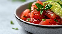 Fresh watermelon salad with lime and mint in ceramic bowl. Healthy summer fruit dish with herbs and citrus garnish for refreshing meal preparation.