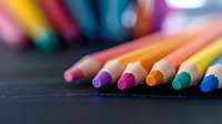 Vibrant colored pencils arranged in row on dark surface with selective focus on tips, creating artistic composition for education and creativity concepts.