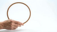 Elderly hand holding a round wooden embroidery hoop against a white background, copy space for craft and needlework projects.