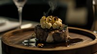 Juicy grilled beef tenderloin steak topped with roasted garlic and blue cheese crumbles in dark balsamic reduction sauce on wooden plate, fine dining presentation.