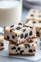 Creamy vanilla cheesecake bars topped with crushed chocolate sandwich cookies on graham cracker crust, stacked in layers with milk glass in background.