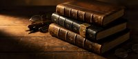 Stack of antique leather-bound books with vintage eyeglasses on rustic wooden table in warm atmospheric lighting for historical education concepts.