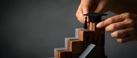 Hands placing a graduation cap on wooden staircase steps, symbolizing academic achievement, career growth, and educational success on dark background.