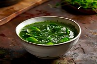 Fresh spinach leaves floating in clear broth served in white ceramic bowl on rustic dark background, dramatic food photography styling for restaurant menu.