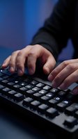 Close-up of male hands typing on black keyboard against blue background. Professional working on computer for business, technology, programming, or office work.