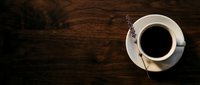Top view of steaming black coffee in white cup and saucer on rustic wooden table with copy space for café, restaurant, or beverage marketing.
