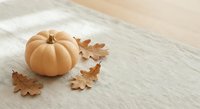 Orange pumpkin with autumn oak leaves on wooden table surface for seasonal decoration and harvest celebration themes.