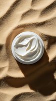 White cosmetic cream in open jar on sand background with natural shadows, minimal skincare product photography for beauty and wellness marketing.