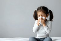 Young Asian girl with pigtails blowing nose into tissue while sitting, showing cold or allergy symptoms against neutral background for health concepts.