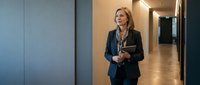 Professional middle-aged Caucasian businesswoman walking confidently through modern office corridor holding documents, corporate executive lifestyle.