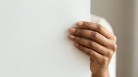 Male hand with medium-deep skin tone touching white wall surface, conveying concepts of support, stability, guidance, or connection for healthcare and wellness applications.