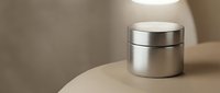 Elegant silver cosmetic jar on a beige surface with soft lighting, showcasing luxury skincare packaging for beauty branding.