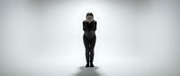 Young woman in black hoodie standing alone in minimalist white studio space with dramatic lighting and shadows for contemporary lifestyle concepts.