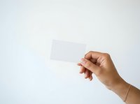 Hand holding blank white card against neutral background, suitable for business card mockups, branding presentations, and promotional material design.