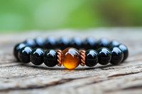 Black onyx beaded bracelet with amber colored centerpiece on wooden surface against blurred green background, spiritual wellness jewelry for meditation.