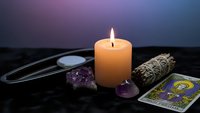 Spiritual healing setup with burning candle, amethyst crystals, sage bundle and tarot cards on dark surface for meditation and wellness practices.