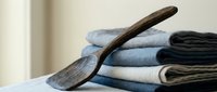 Wooden laundry paddle resting on stack of folded cotton towels in neutral tones for traditional household cleaning and textile care concepts.