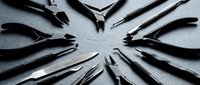 Professional black pliers and cutting tools arranged in circular pattern on textured surface for crafting, jewelry making, and precision work applications.