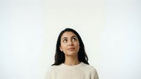 Young woman with long dark hair and South Asian ethnicity wearing a cream-colored ribbed sweater, looking upward thoughtfully against a white background. Isolated portrait suitable for business, lifestyle, and editorial design projects.