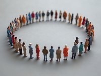 Diverse group of miniature people standing in circle formation on white surface, representing community, unity and social connection in business or society.
