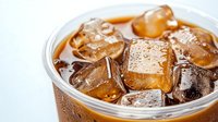 Refreshing cola drink with ice cubes in clear plastic cup, closeup view showing carbonated beverage and melting ice against white background.