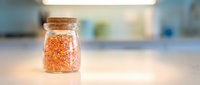 Red lentils in glass jar with cork lid on blurred kitchen counter background, suitable for food storage, cooking, and healthy eating concepts.