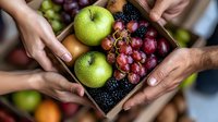 Fresh green apples, ripe blackberries and red grapes in wooden box held by hands, representing healthy eating, farm market produce and seasonal harvest.