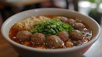 Traditional Vietnamese pho soup with beef meatballs, rice noodles and fresh herbs in rich brown broth served in white ceramic bowl for authentic cuisine.