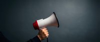 Hand holding white and red megaphone against dark background for communication, announcement, marketing campaigns and public speaking concepts.