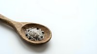 Wooden spoon filled with sea salt and black peppercorns on white background, suitable for cooking, food styling, culinary blogs and recipe websites.