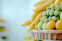 Fresh yellow bananas and green grapes arranged in wicker basket, selective focus on ripe tropical fruits creating soft dreamy composition with blurred background.