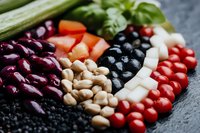 Fresh colorful ingredients arranged in rows including kidney beans, chickpeas, black olives, feta cheese and cherry tomatoes on dark background for Mediterranean cuisine.