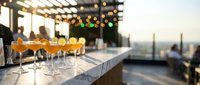 Elegant cocktails on marble bar counter at upscale rooftop terrace during golden hour sunset with city skyline backdrop for hospitality and dining concepts.