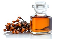Small glass bottle with amber liquid and fresh sea buckthorn berries branch on white background, natural organic cosmetic ingredient for skincare products.