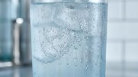 Refreshing glass of sparkling water with ice cubes and bubbles on clean white surface for healthy lifestyle and hydration concepts.