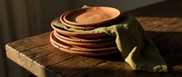 Stacked crepes with olive green linen napkin on rustic wooden board, warm golden lighting, breakfast or dessert preparation.