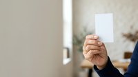 Close-up of hand holding blank white card in modern office environment, suitable for business communication, voting, feedback, or promotional messaging concepts.