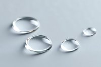 Clear water droplets on light gray surface creating natural lens effect with soft shadows and reflections.